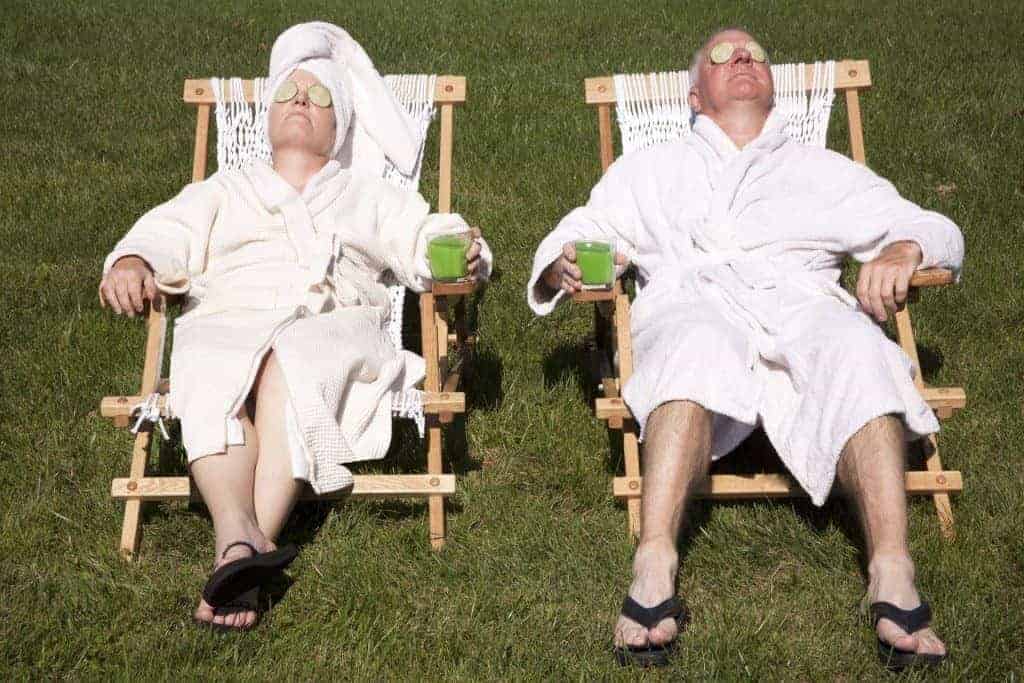 an older man and woman sitting in the sun in bathrobes with cucumbers on their eyes