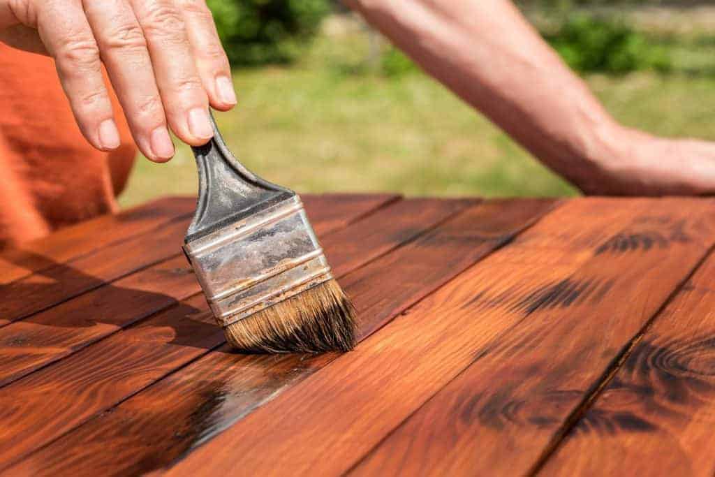 Person staining wood mobile home patio with a paint brush