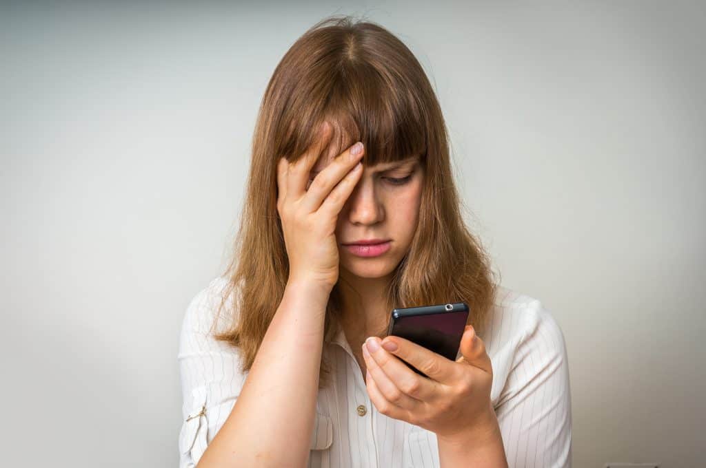 Stressed and confused woman holding and looking at cell phone
