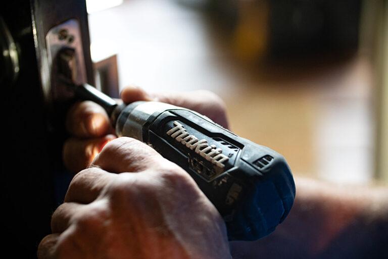 man tightening a door hinge with electric drill