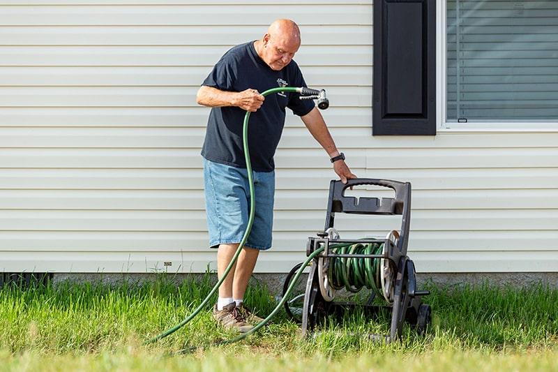 man using hose to clean mobile home siding and windows