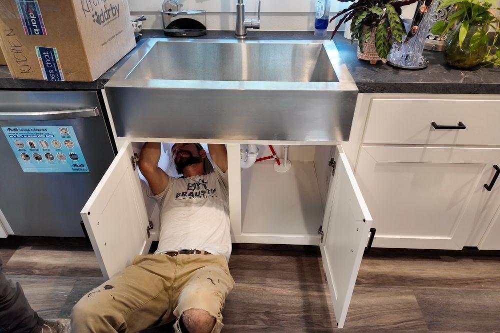 Service team under a farmhouse sink fixing an issue reported by a new homeowner